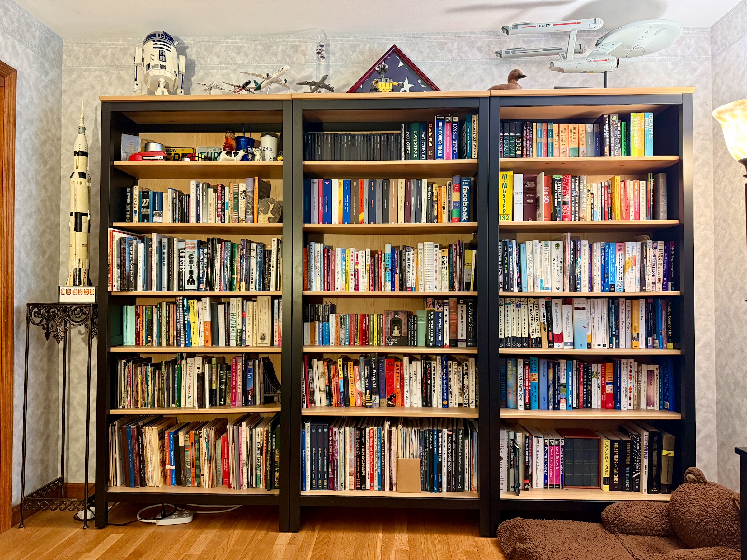 Three new black bookcases with light wood shelves filled with books in Mike’s office, with model spacecraft and other collectibles displayed on top